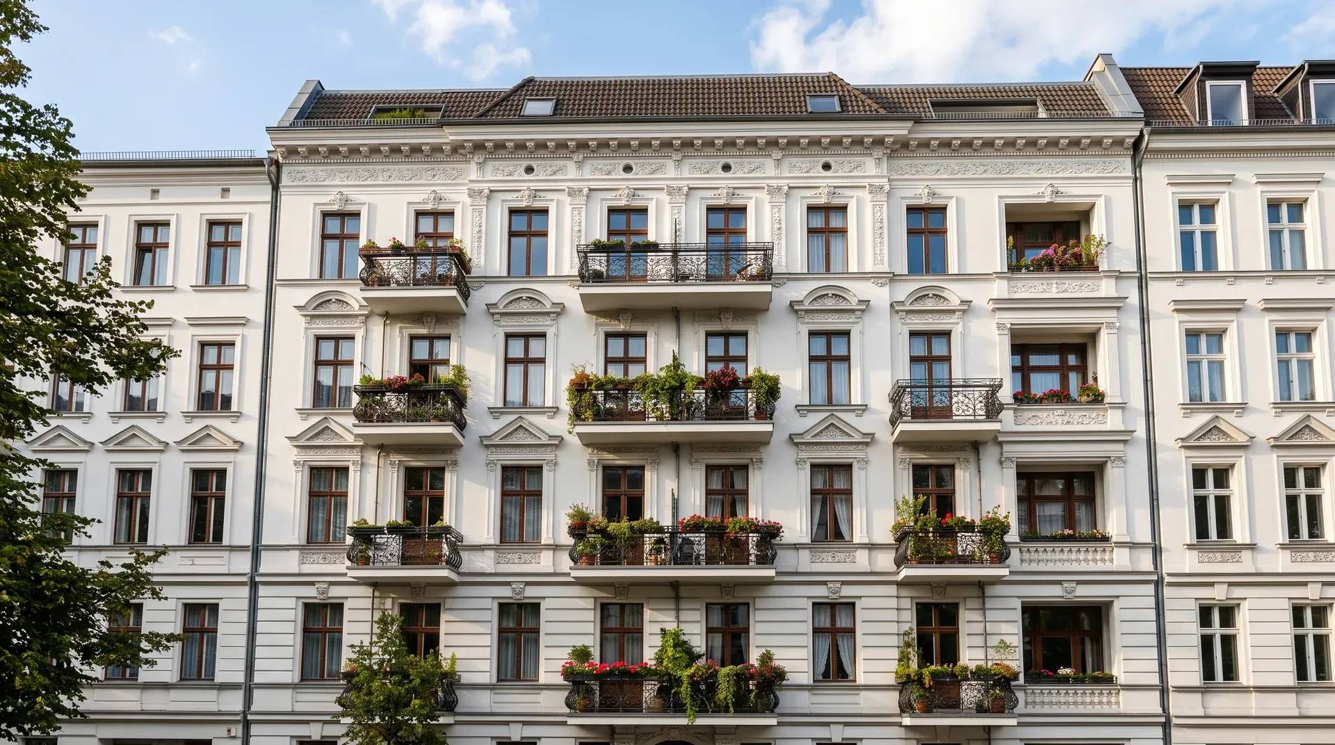 Weiße Altbaufassade eines Mehrfamilienhauses mit schmiedeeisernen Balkonen und Blumenkästen
