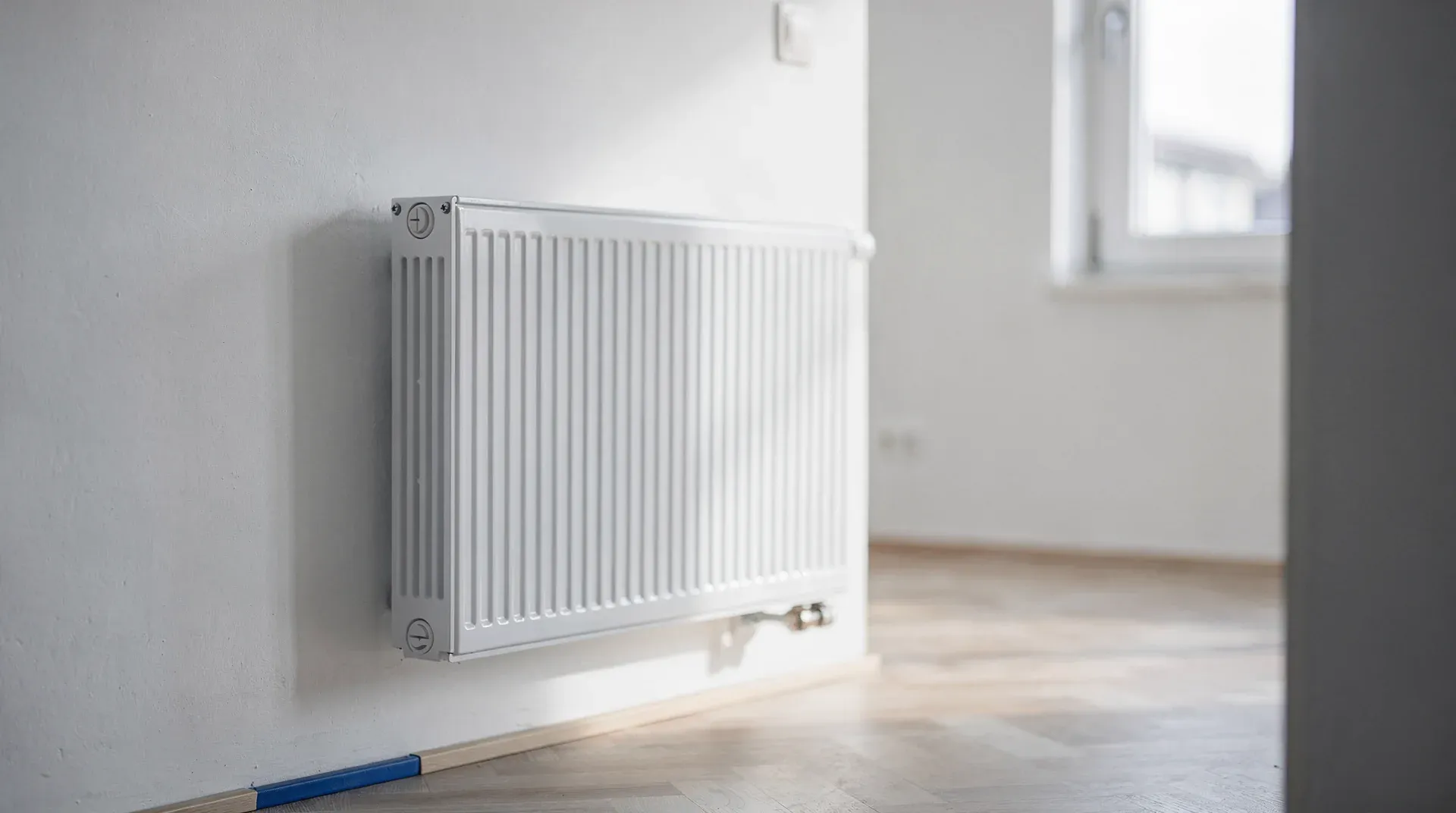 Weißer Heizkörper an der Wand einer leeren, renovierten Wohnung mit Parkettboden und Fenster